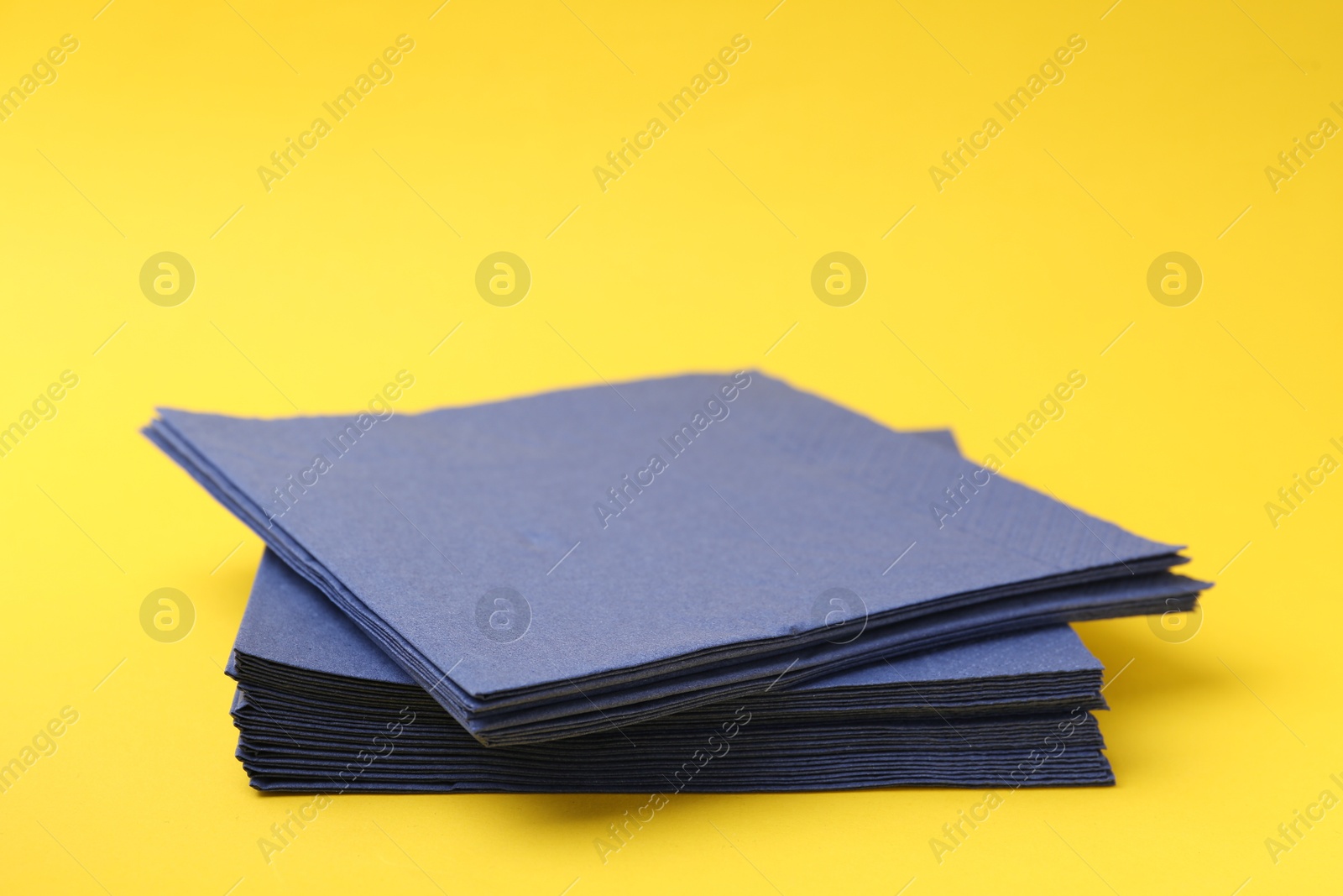 Stack of blue handkerchiefs on yellow background, closeup. Space for text Photo of Stack of blue handkerchiefs on yellow background, closeup. Space for text