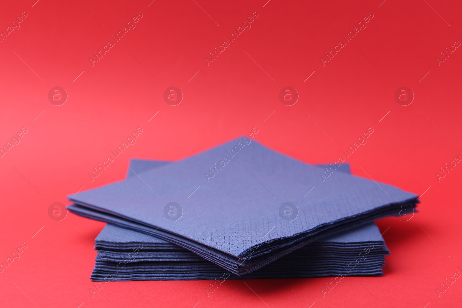 Stack of blue handkerchiefs on red background, closeup. Space for text Photo of Stack of blue handkerchiefs on red background, closeup. Space for text