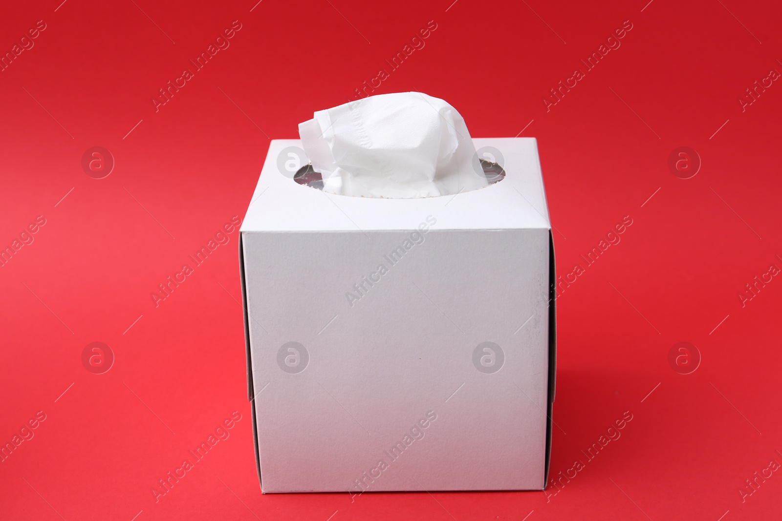 Box with paper handkerchiefs on red background Photo of Box with paper handkerchiefs on red background