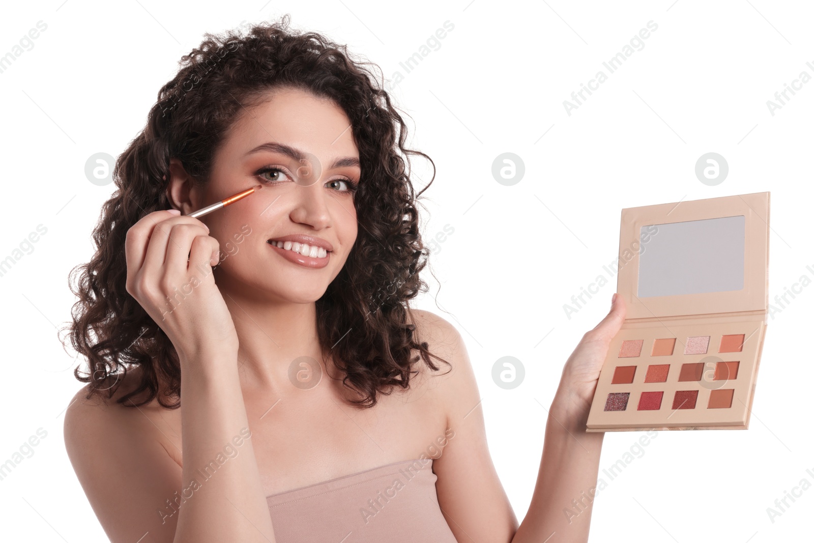 Smiling woman with eyeshadow palette and brush applying makeup on white background Photo of Smiling woman with eyeshadow palette and brush applying makeup on white background