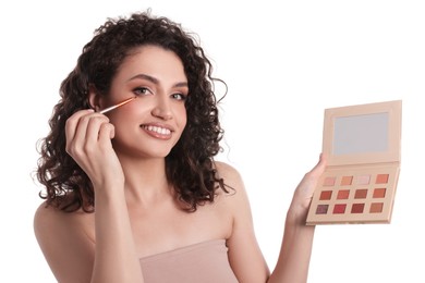 Photo of Smiling woman with eyeshadow palette and brush applying makeup on white background