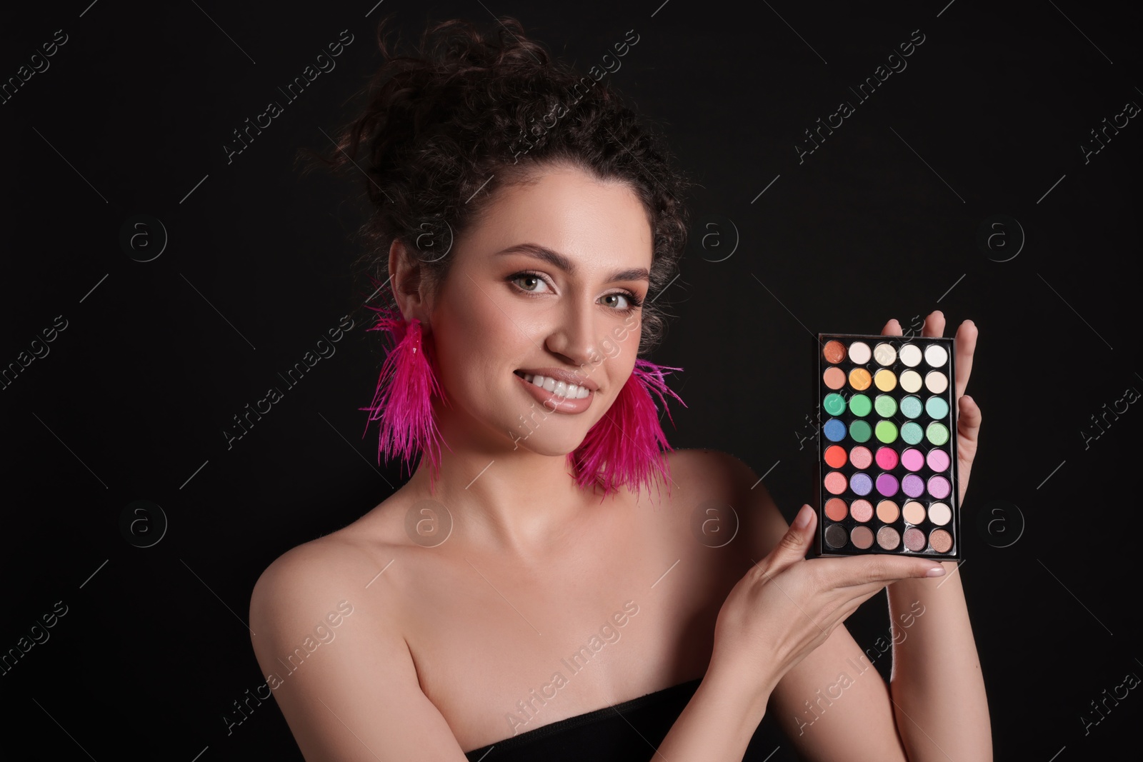 Smiling woman with bright eyeshadow palette on black background Photo of Smiling woman with bright eyeshadow palette on black background