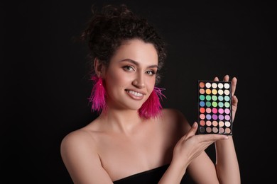 Photo of Smiling woman with bright eyeshadow palette on black background
