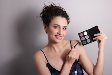 Photo of Smiling woman with eyeshadow palette and brush on grey background. Space for text