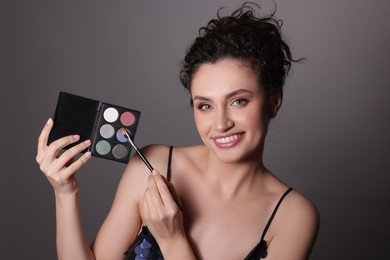 Photo of Smiling woman with eyeshadow palette and brush on grey background