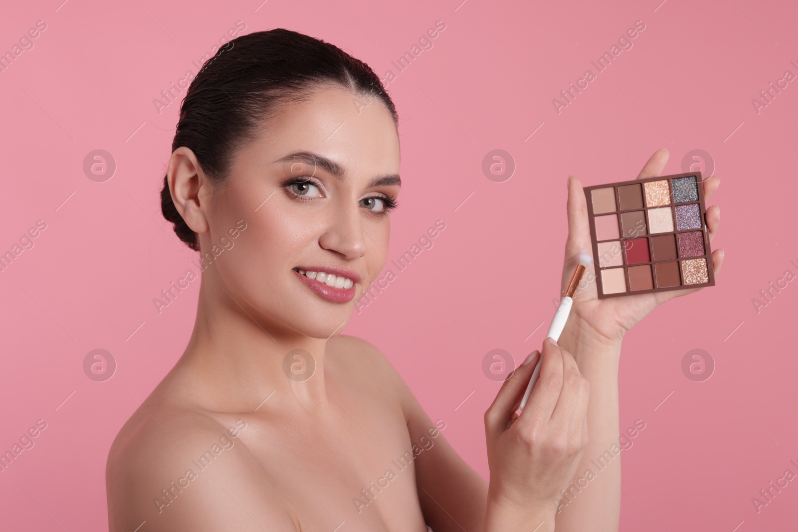 Woman with eyeshadow palette and brush on pink background Photo of Woman with eyeshadow palette and brush on pink background