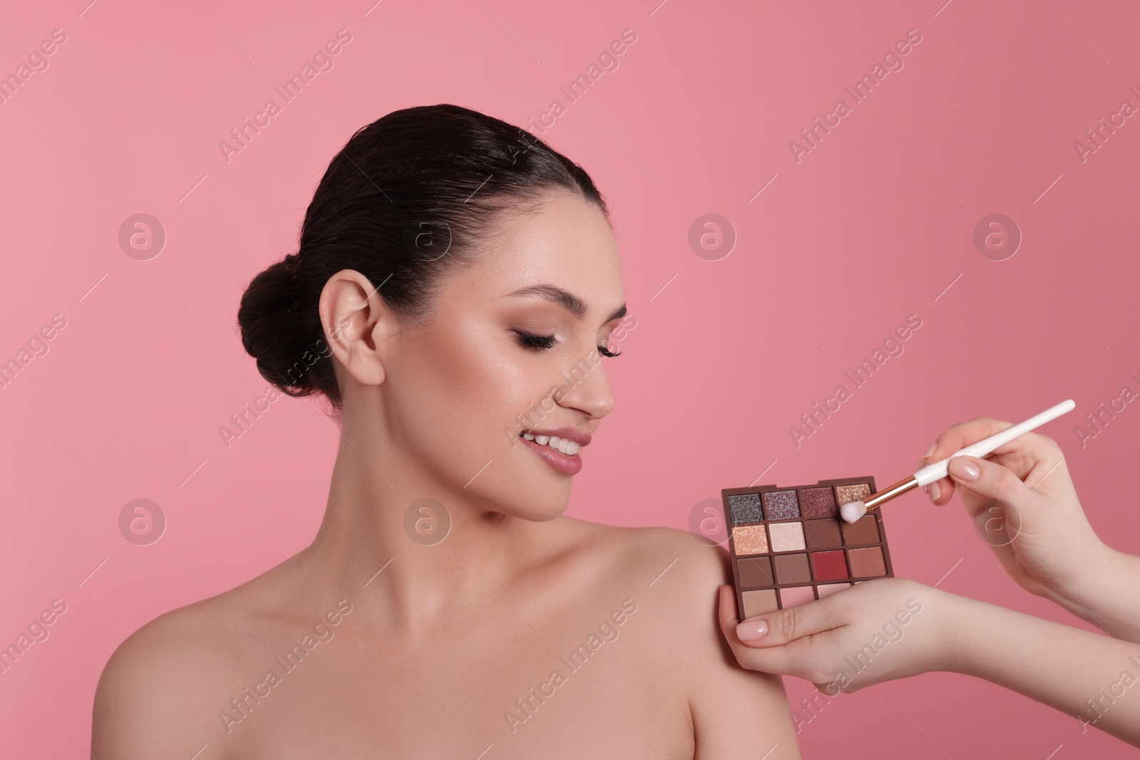 Makeup artist with eyeshadow palette, brush and smiling woman on pink background, closeup Photo of Makeup artist with eyeshadow palette, brush and smiling woman on pink background, closeup