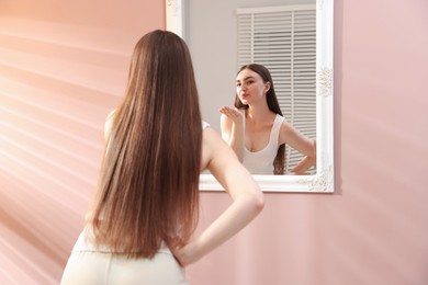 Photo of Beautiful woman blowing kiss near mirror indoors