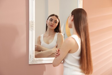 Photo of Beautiful woman looking at herself in mirror indoors