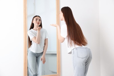 Photo of Beautiful woman blowing kiss near mirror indoors