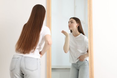 Photo of Beautiful woman blowing kiss near mirror indoors