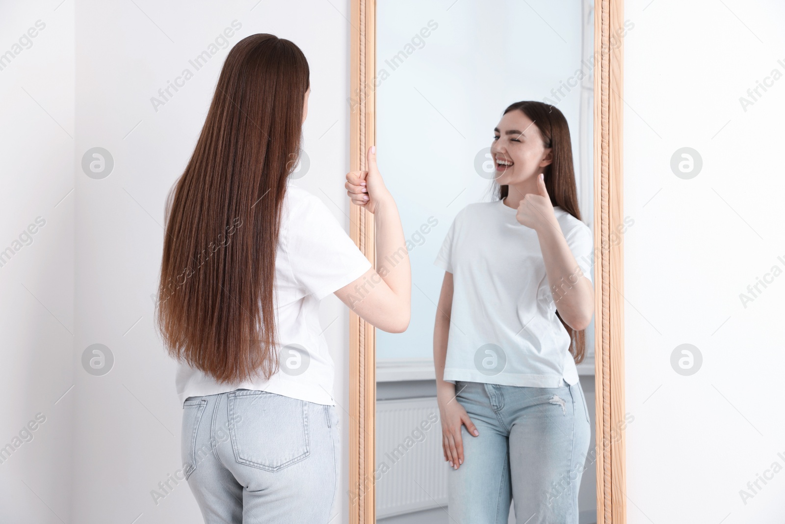 Beautiful woman showing thumbs up near mirror indoors Photo of Beautiful woman showing thumbs up near mirror indoors