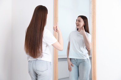Photo of Beautiful woman showing thumbs up near mirror indoors