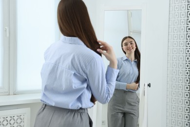 Photo of Beautiful woman looking at herself in mirror indoors