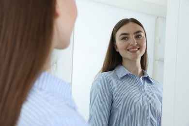 Photo of Beautiful woman looking at herself in mirror indoors