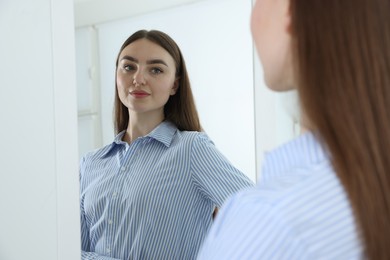 Photo of Beautiful woman looking at herself in mirror indoors