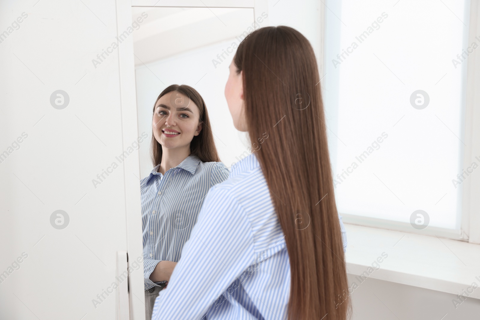 Beautiful woman looking at herself in mirror indoors Photo of Beautiful woman looking at herself in mirror indoors