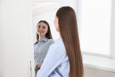 Photo of Beautiful woman looking at herself in mirror indoors