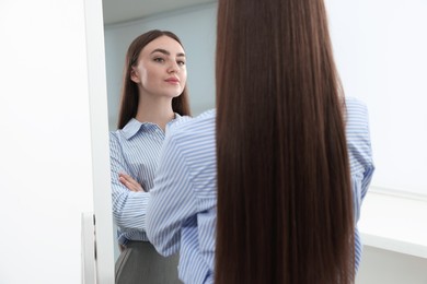 Photo of Beautiful woman looking at herself in mirror indoors