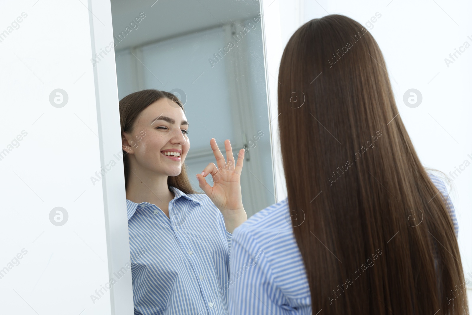 Beautiful woman showing ok gesture near mirror indoors Photo of Beautiful woman showing ok gesture near mirror indoors