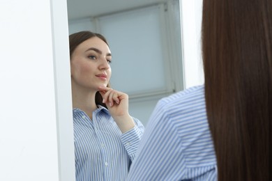 Photo of Beautiful woman looking at herself in mirror indoors