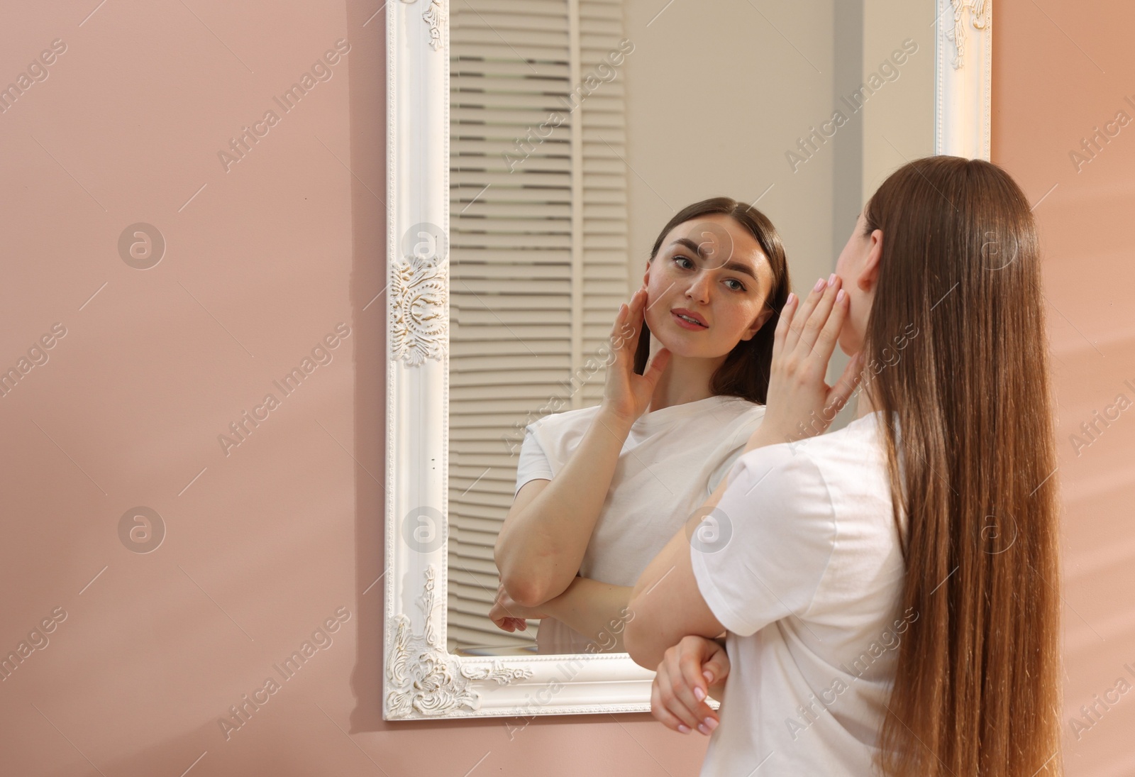 Beautiful woman looking at herself in mirror indoors, space for text Photo of Beautiful woman looking at herself in mirror indoors, space for text