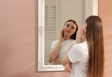 Photo of Beautiful woman looking at herself in mirror indoors, space for text