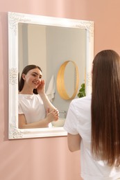 Photo of Beautiful woman looking at herself in mirror indoors
