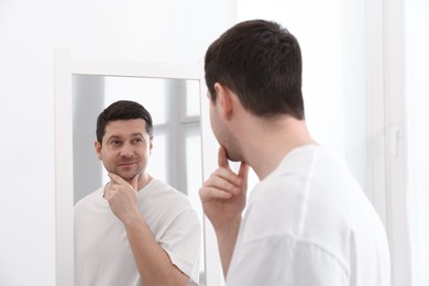 Photo of Handsome man looking at himself in mirror indoors