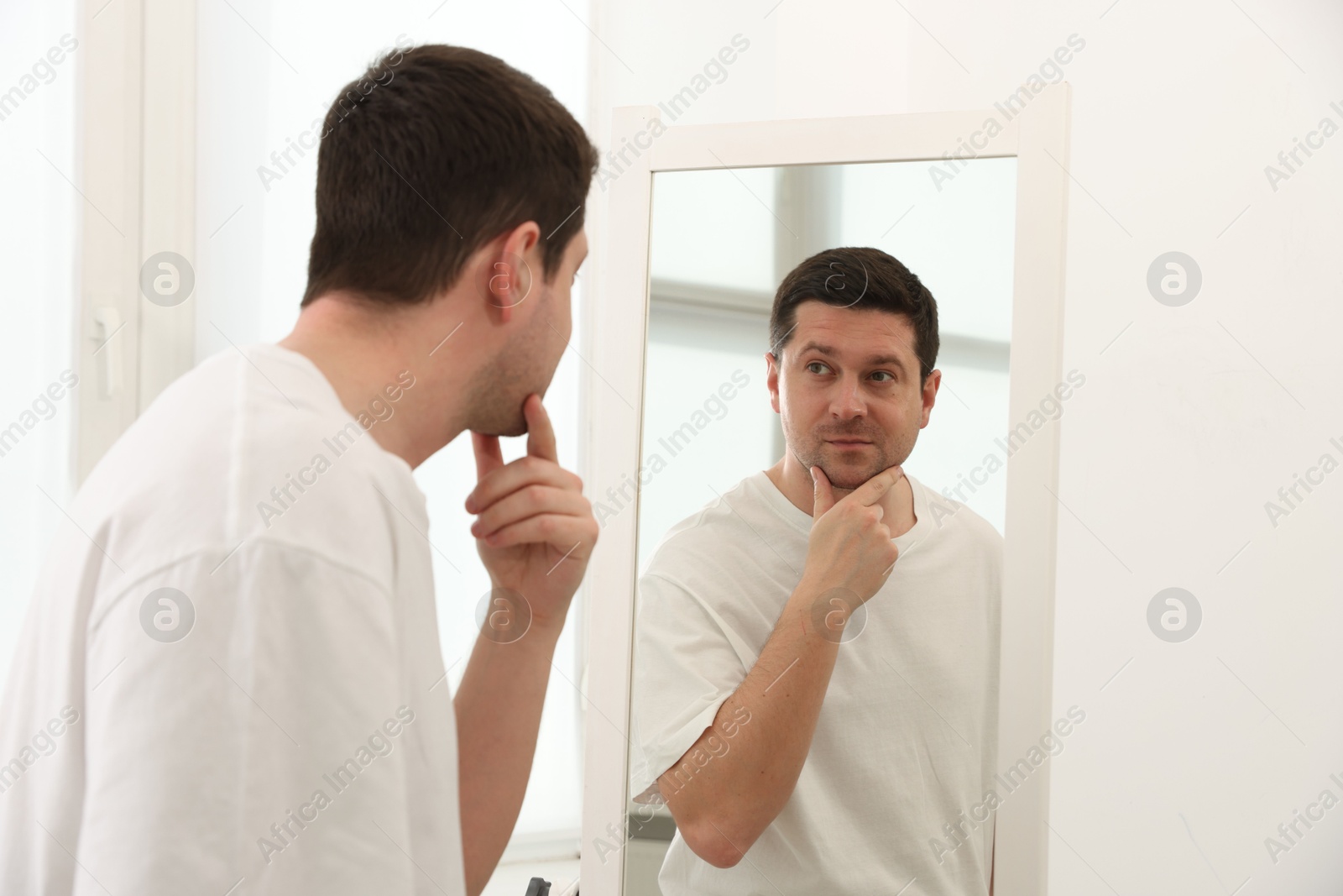 Handsome man looking at himself in mirror indoors Photo of Handsome man looking at himself in mirror indoors