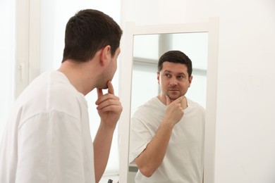 Photo of Handsome man looking at himself in mirror indoors