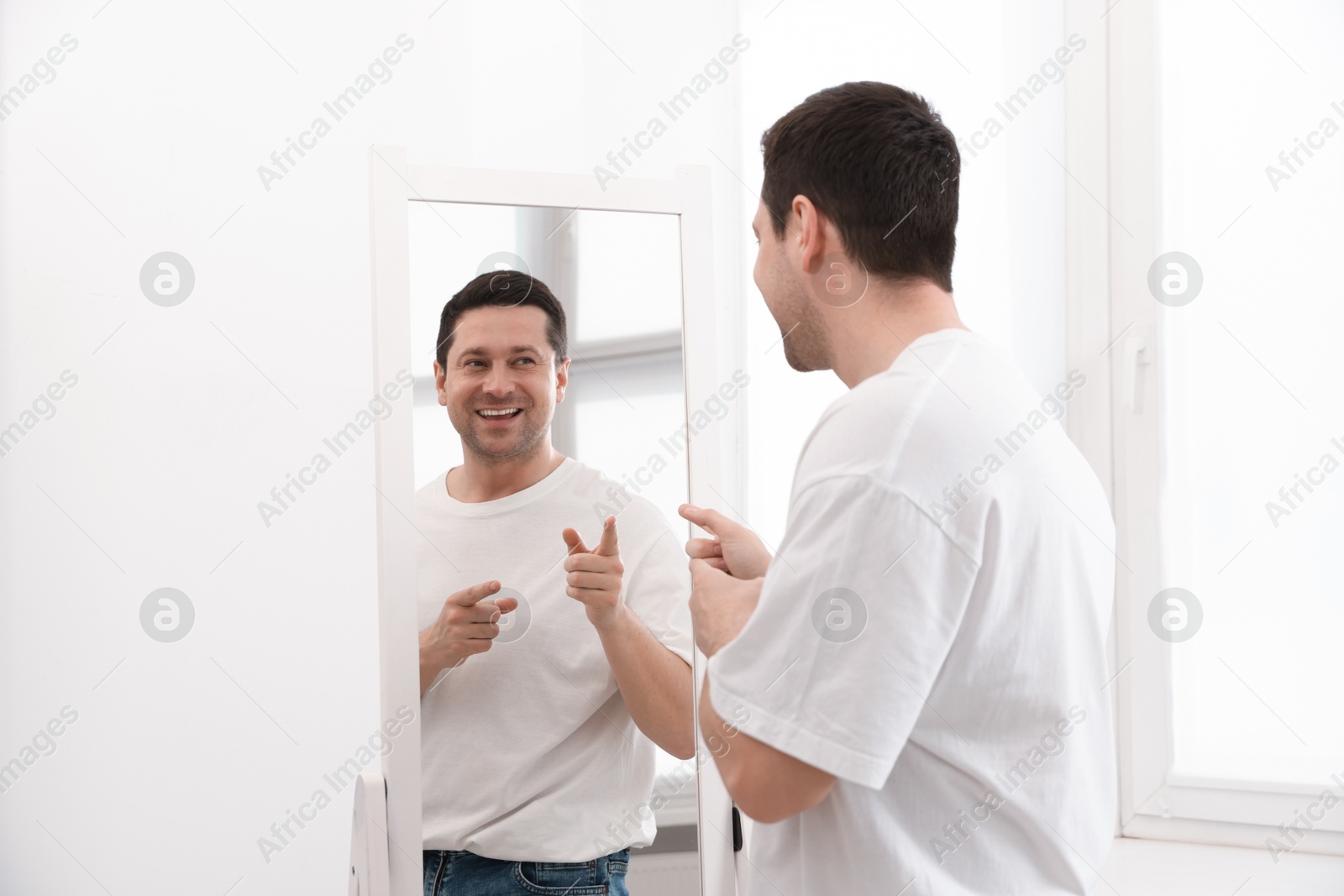 Handsome man looking at himself in mirror indoors Photo of Handsome man looking at himself in mirror indoors