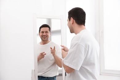 Photo of Handsome man looking at himself in mirror indoors