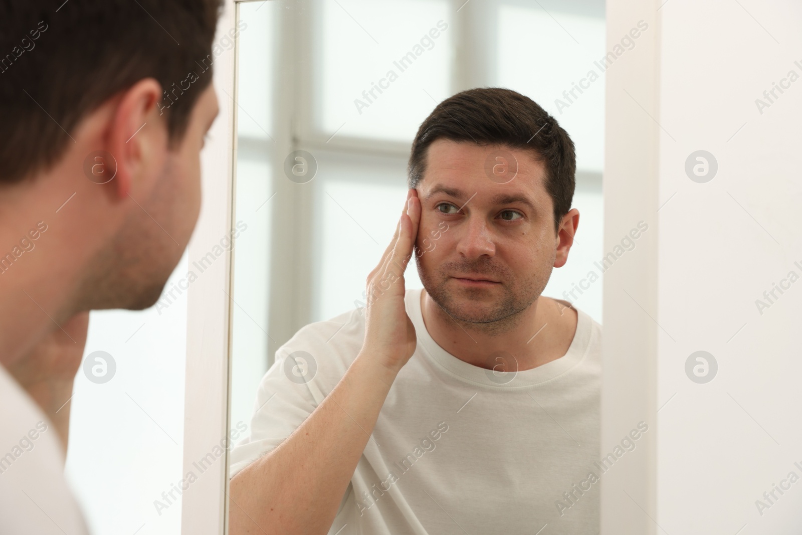 Handsome man looking at himself in mirror indoors Photo of Handsome man looking at himself in mirror indoors
