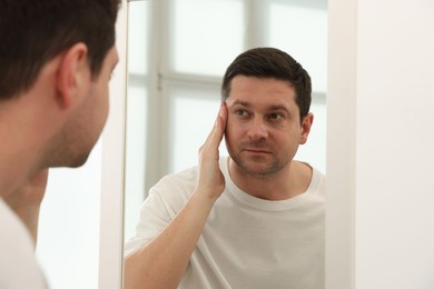 Photo of Handsome man looking at himself in mirror indoors