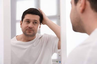 Photo of Handsome man looking at himself in mirror indoors
