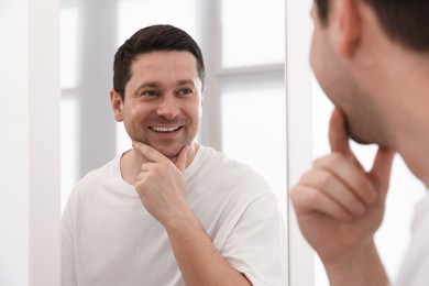 Photo of Handsome man looking at himself in mirror indoors