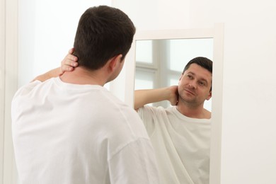 Photo of Handsome man looking at himself in mirror indoors