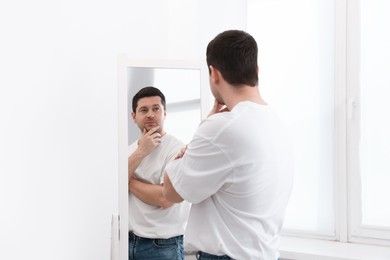 Photo of Handsome man looking at himself in mirror indoors