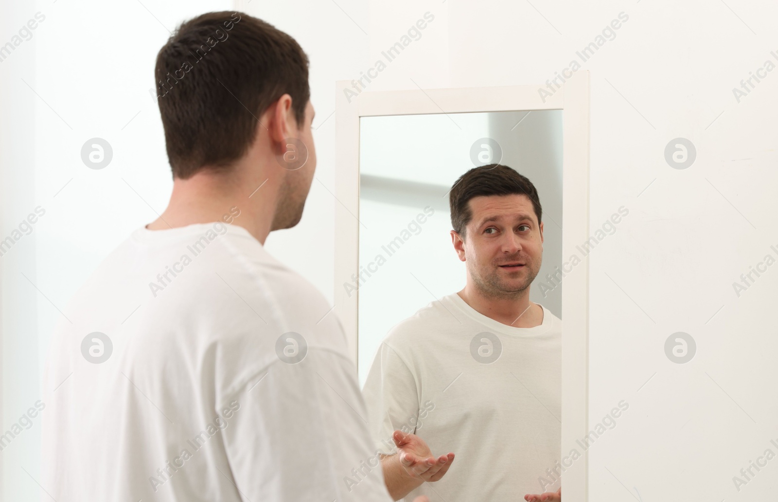 Handsome man looking at himself in mirror indoors Photo of Handsome man looking at himself in mirror indoors