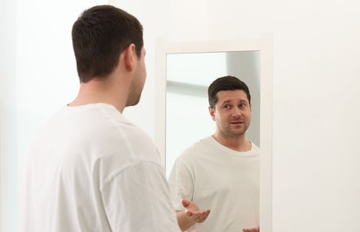 Photo of Handsome man looking at himself in mirror indoors