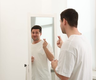 Photo of Handsome man showing heart gesture near mirror indoors
