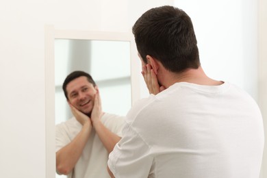 Photo of Handsome man looking at himself in mirror indoors