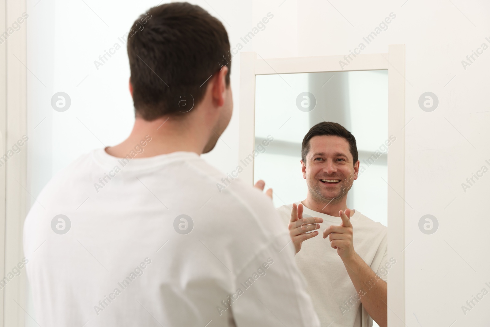 Handsome man looking at himself in mirror indoors Photo of Handsome man looking at himself in mirror indoors