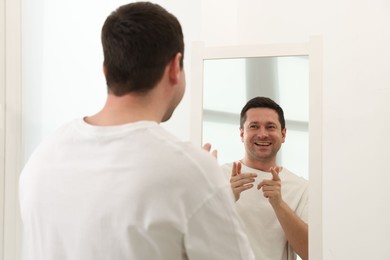 Photo of Handsome man looking at himself in mirror indoors