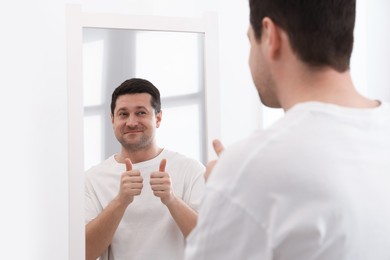 Photo of Handsome man showing thumbs up near mirror indoors