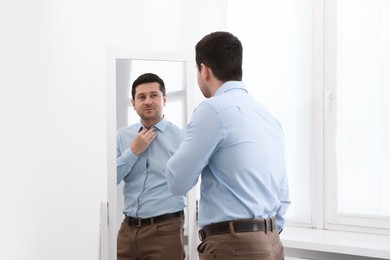 Photo of Handsome man looking at himself in mirror indoors