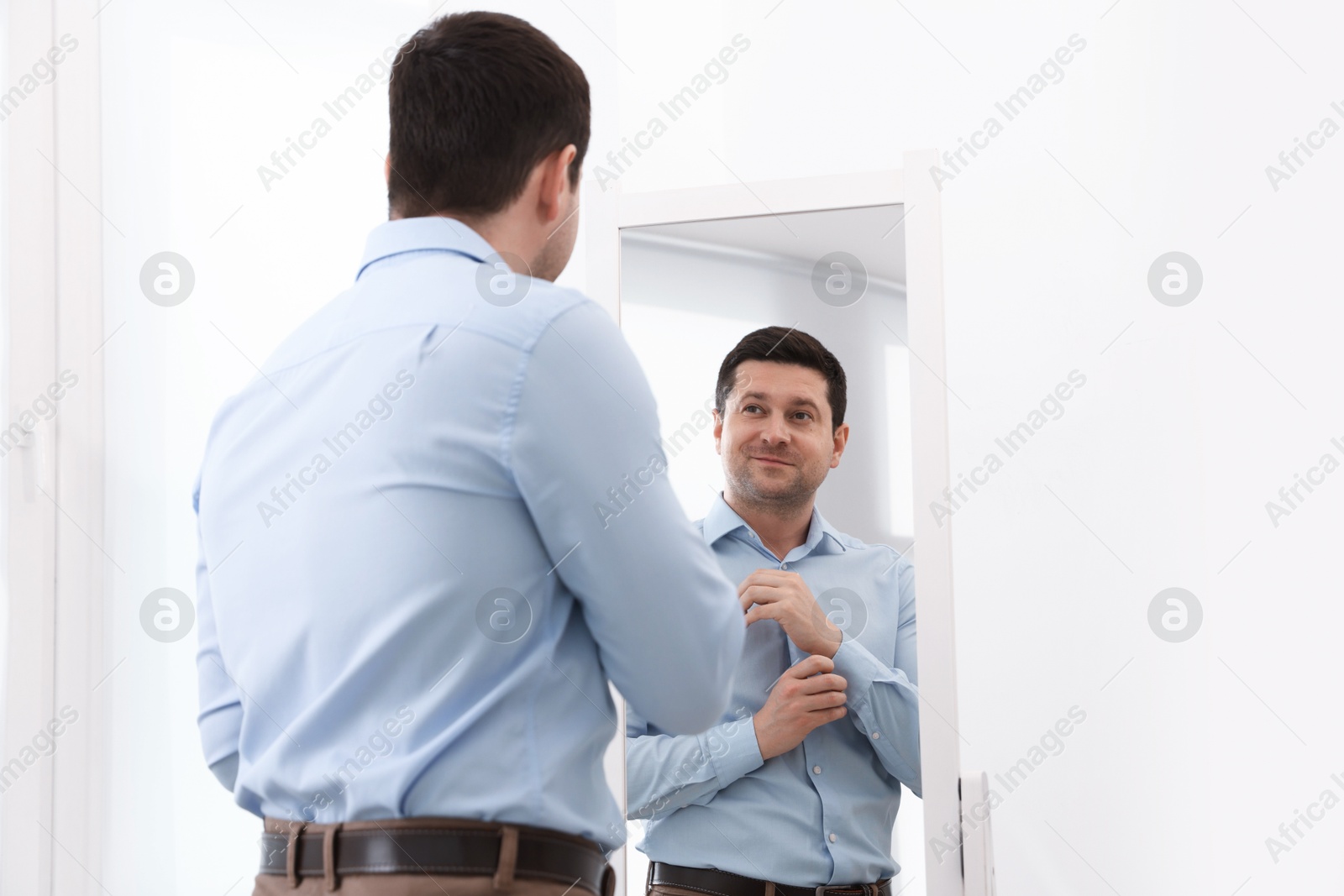 Handsome man looking at himself in mirror indoors Photo of Handsome man looking at himself in mirror indoors