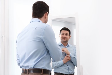 Photo of Handsome man looking at himself in mirror indoors