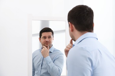Photo of Handsome man looking at himself in mirror indoors